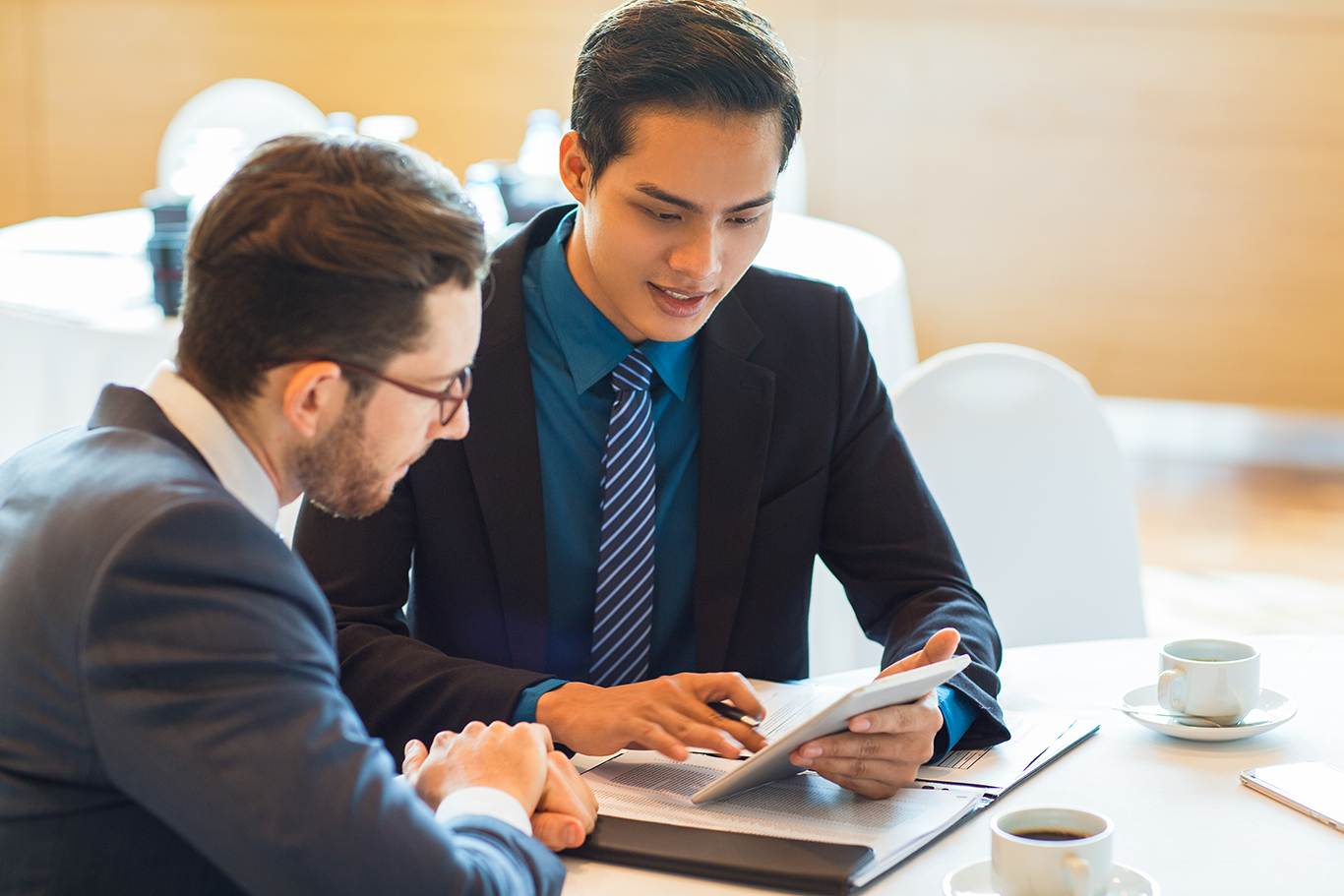 Two Content Business Partners Discussing Issue Closeup of two content adult business men sitting at table, using tablet computer, working with documents and discussing them in cafe